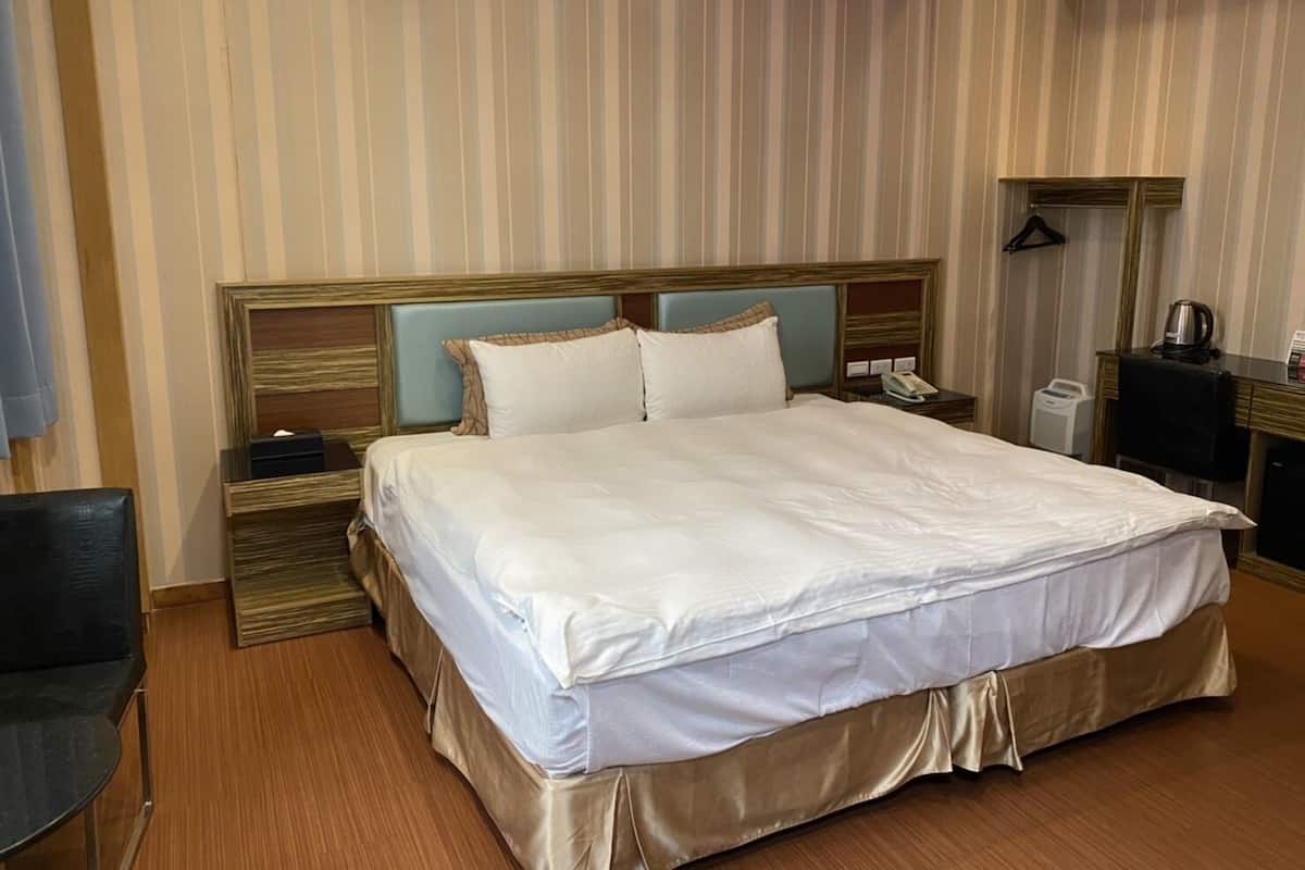 Une chambre d’hôtel avec un grand lit, une tête de lit en bois, des tables de chevet, un bureau et un porte-manteau mural.