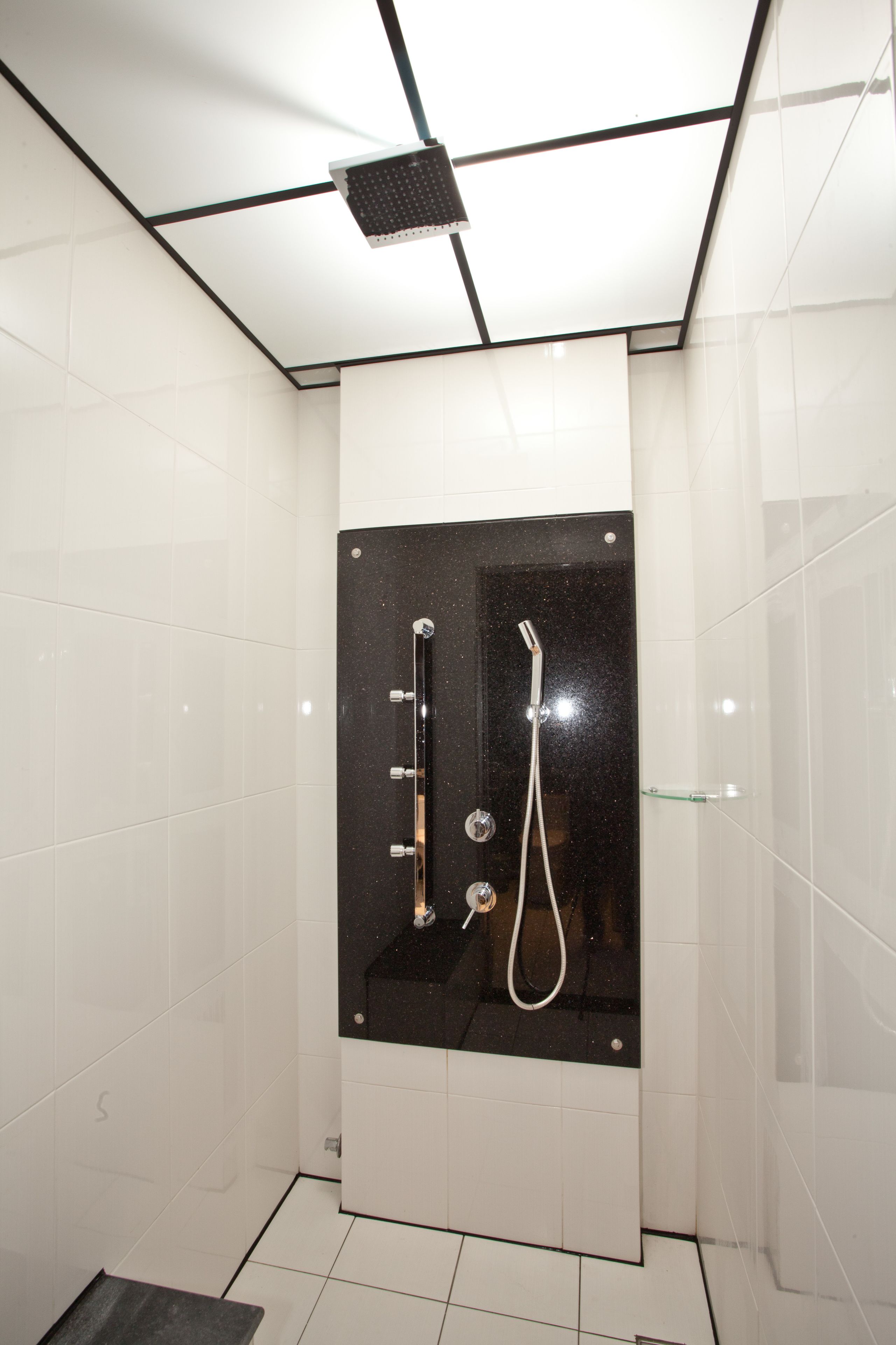 Un baño moderno con azulejos blancos, un box de ducha negro y una puerta de cristal.