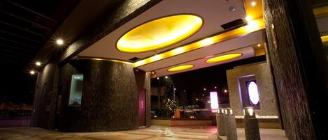 Una entrada de hotel moderna con luminarias circulares, piso de baldosas y fachada de piedra.