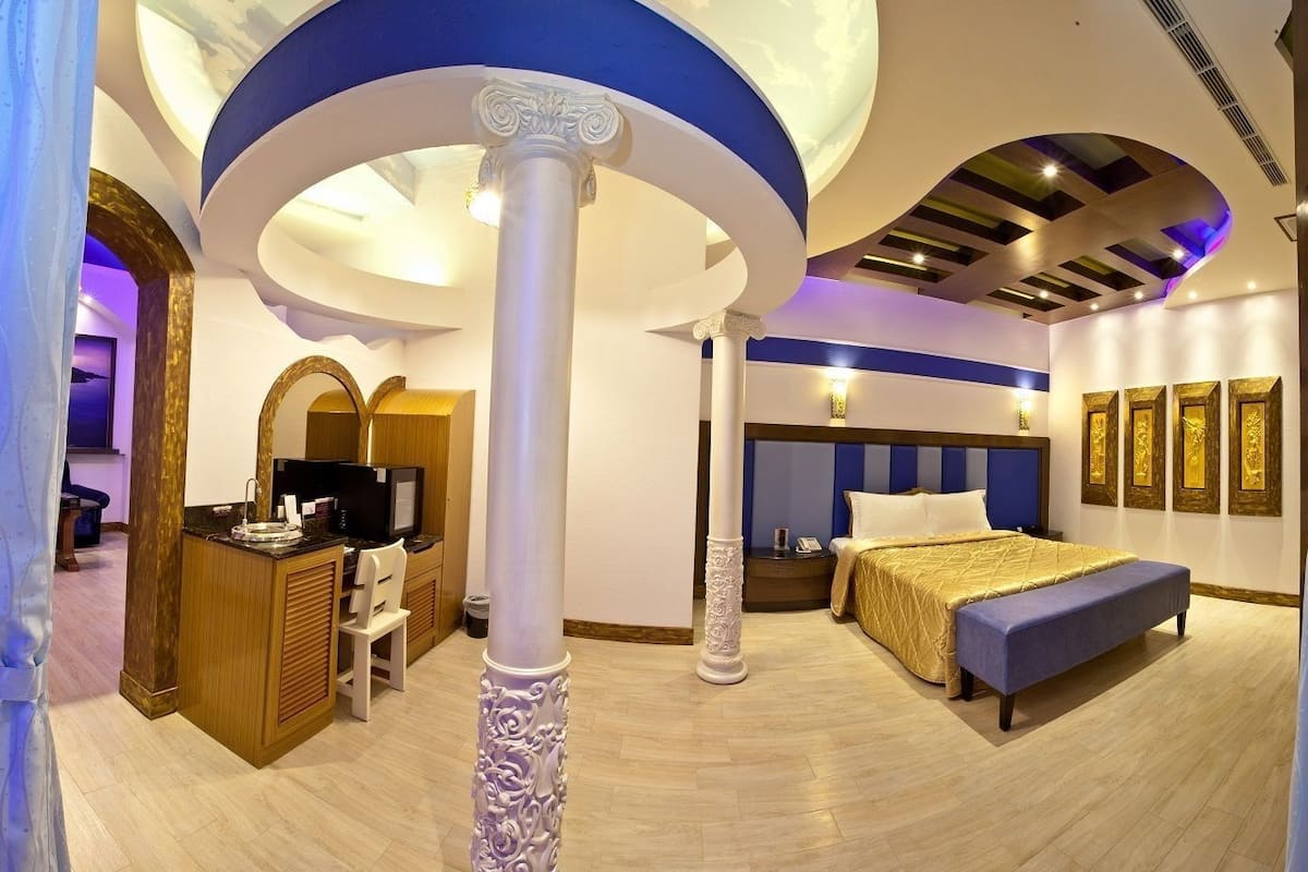 Une chambre d’hôtel avec un grand lit, un bureau avec un ordinateur, une télévision et un plafond décoratif.