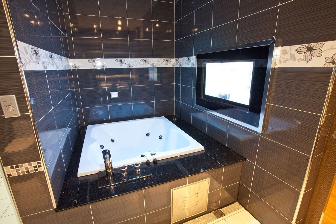 A modern bathroom with a large bathtub, dark tiled walls, and a built-in TV.