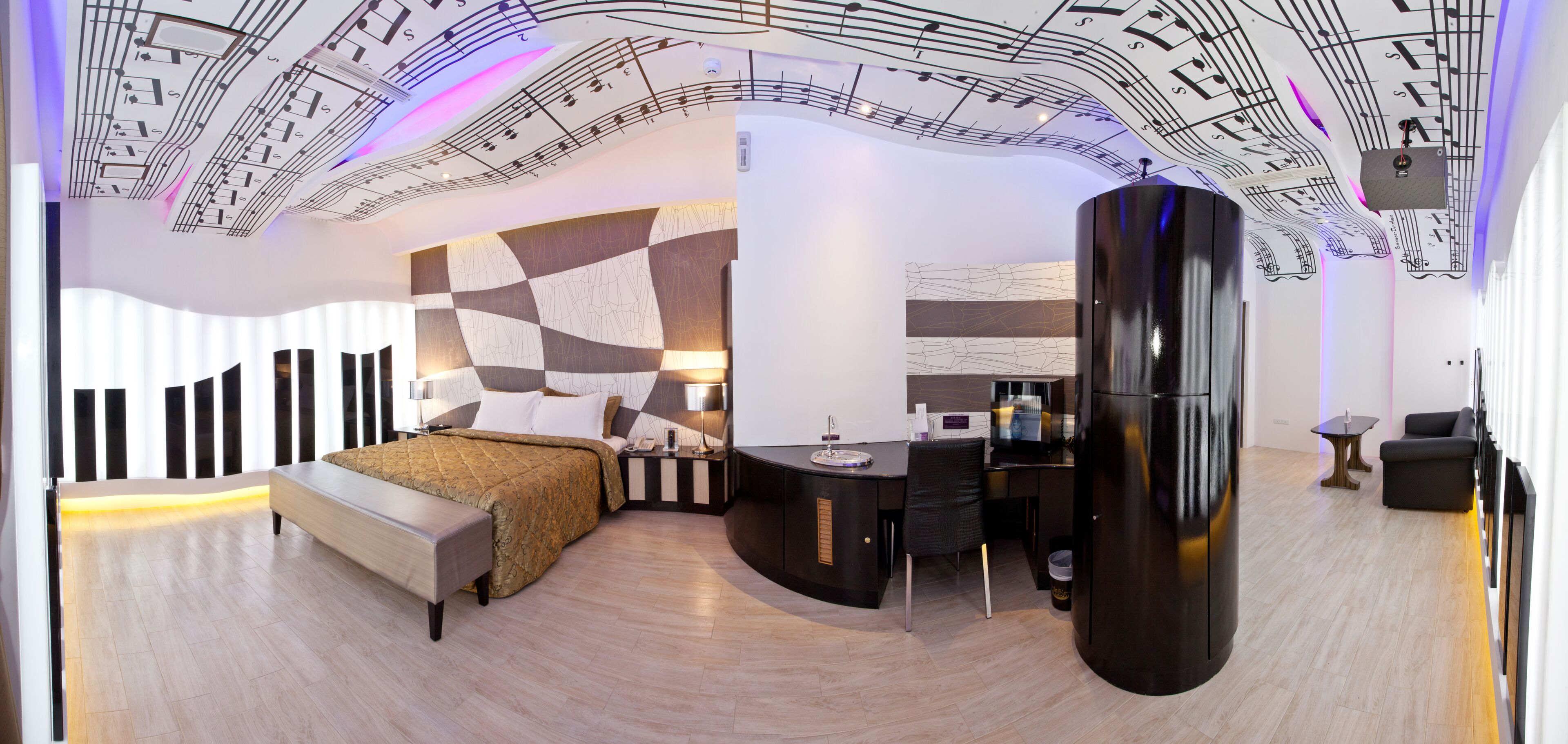 A modern bedroom with a curved ceiling, a bed with a patterned headboard, a desk with a computer, and a large black wardrobe.