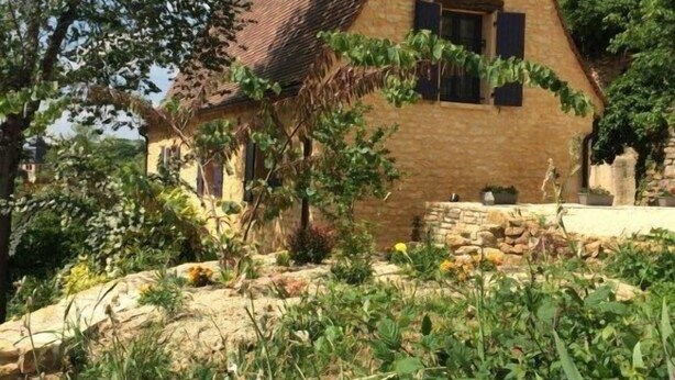 A traditional stone house with a triangular roof, surrounded by lush greenery and a stone pathway. - House in the heart of the medieval city, ideal location and dream land (SARLAT)