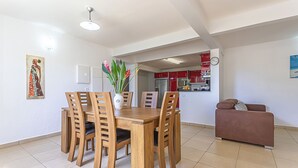 A dining area with a wooden table and chairs, a vase with flowers, and a kitchen in the background. - Bottom of villa with pool (le Moule)