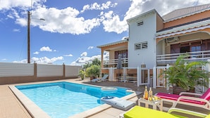 A swimming pool with lounge chairs and a table, surrounded by a building with a balcony. - Bottom of villa with pool (le Moule)