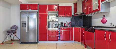 A kitchen with red cabinets, a stainless steel refrigerator, a coffee maker, and a kettle.