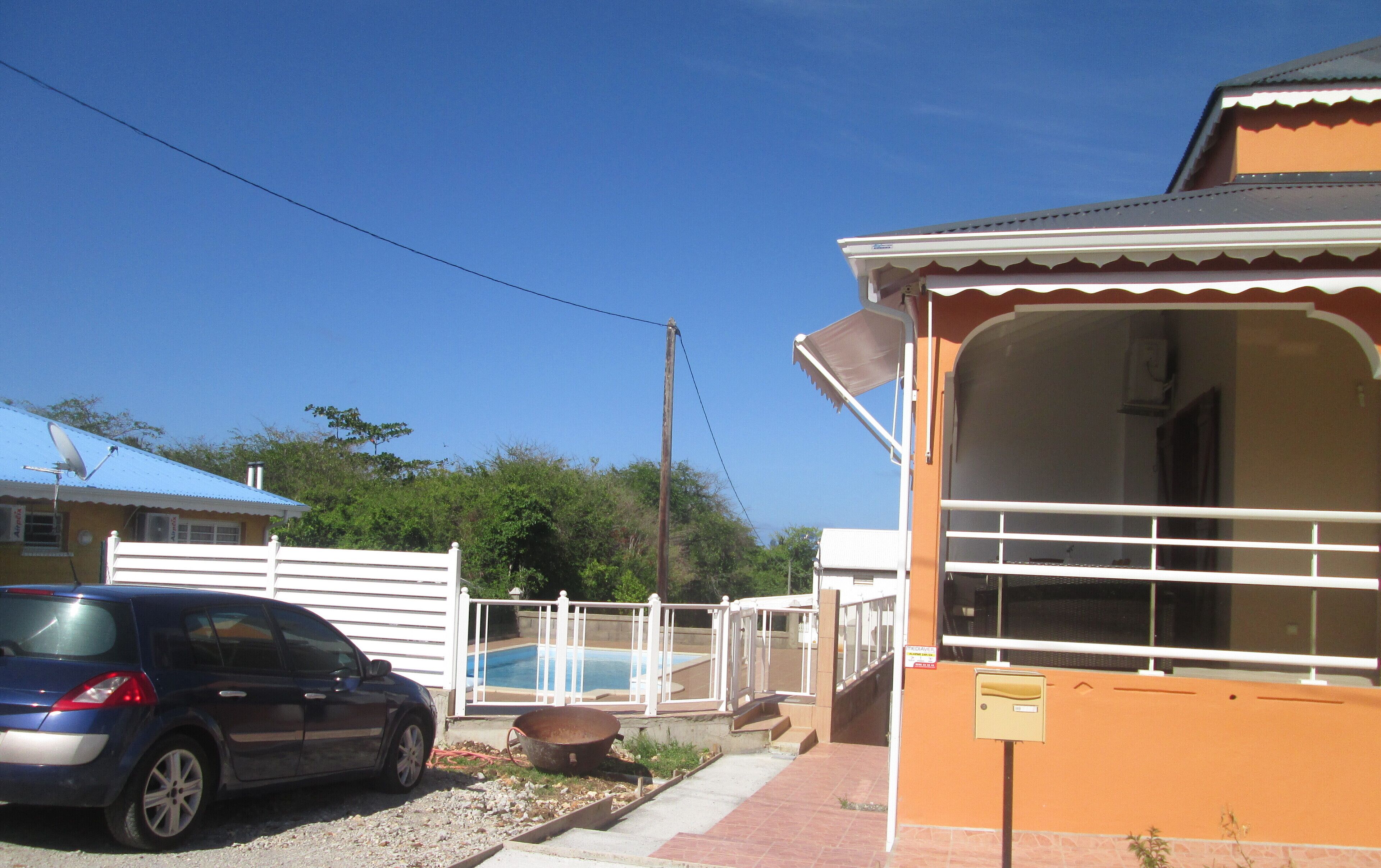 A residential area with a blue car parked in front of a house, a swimming pool, and a mailbox.