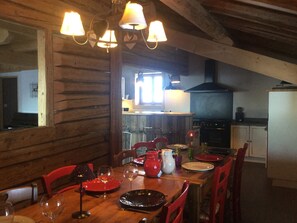 A wooden dining area with a table set for four, a kitchen in the background, and a large mirror on the left wall.
