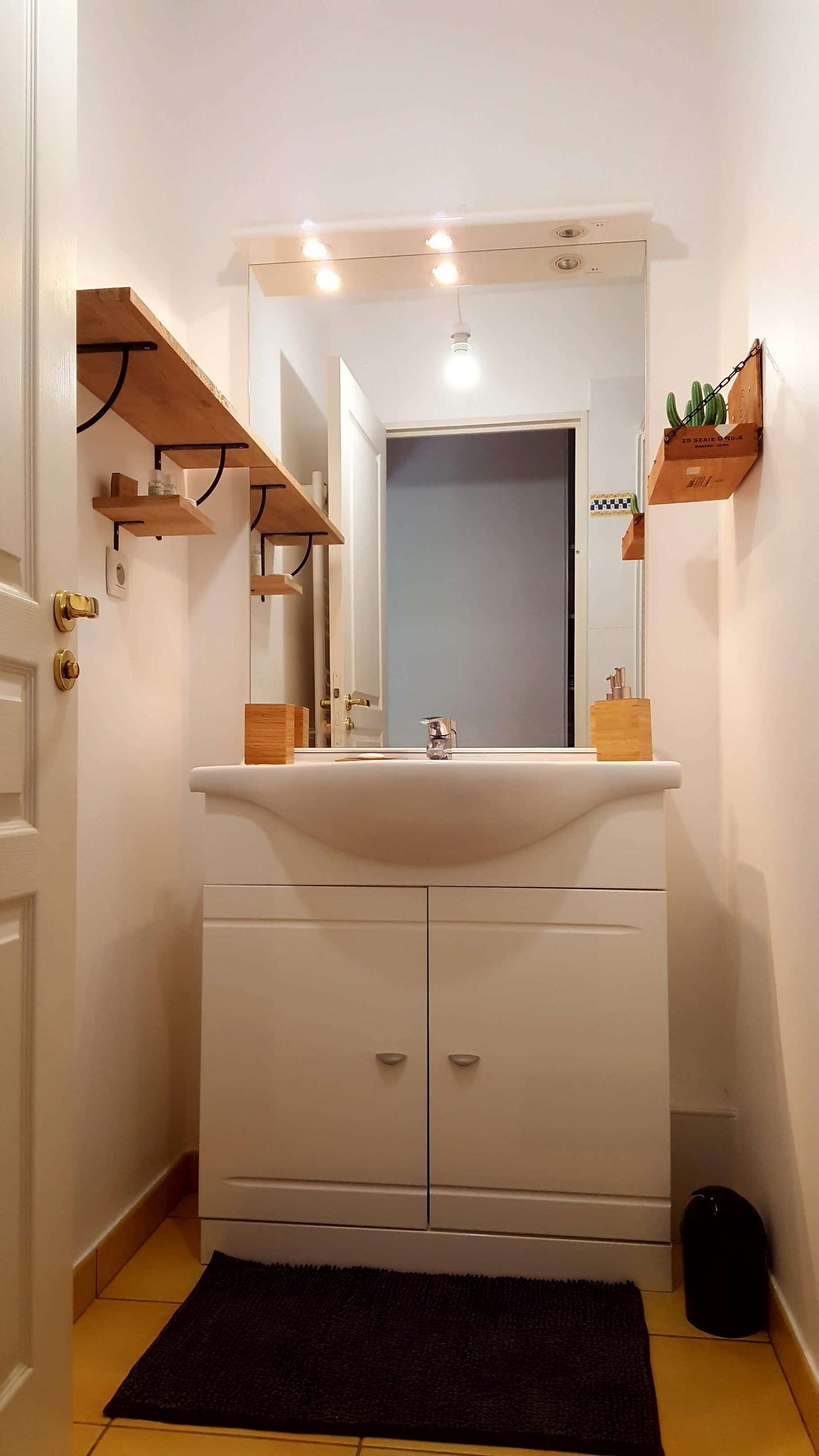 Een badkamer met een witte wasbak, een spiegel erboven en houten planken aan de muur.