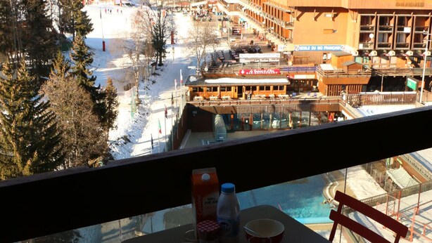 Un balcon avec une table, des chaises et une vue sur un paysage enneigé, avec des bâtiments et une piscine.