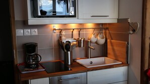 Une cuisine compacte équipée d’un four à micro-ondes, d’une machine à café et d’un porte-ustensiles suspendu.