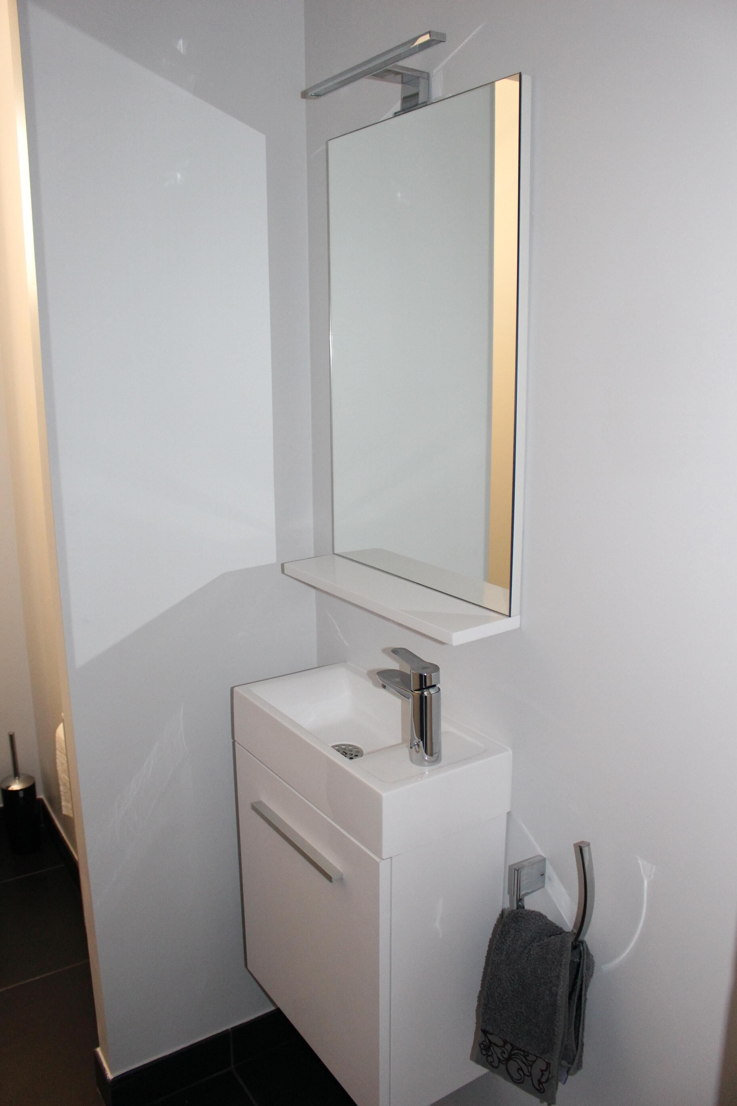 Une salle de bain moderne avec un meuble-lavabo blanc, un miroir et un porte-serviettes.