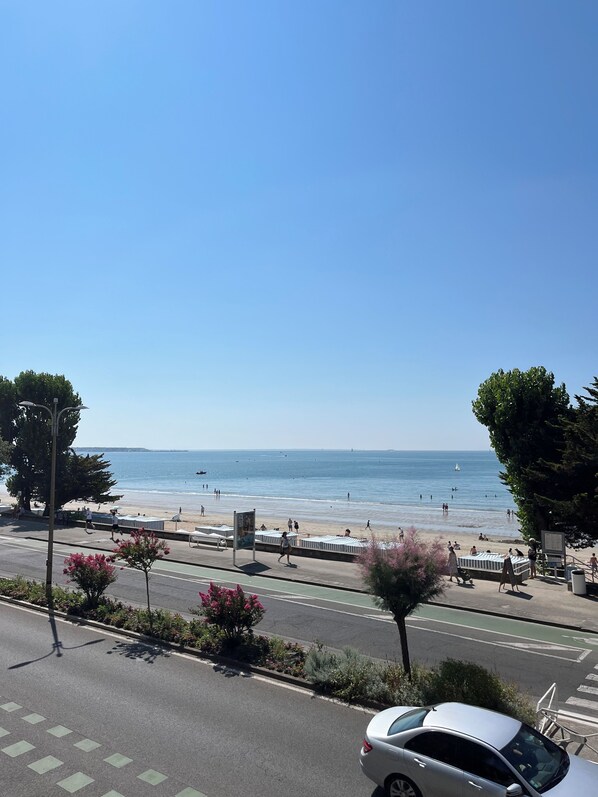A coastal road with a beach in the background, a pedestrian path, and a parked car.