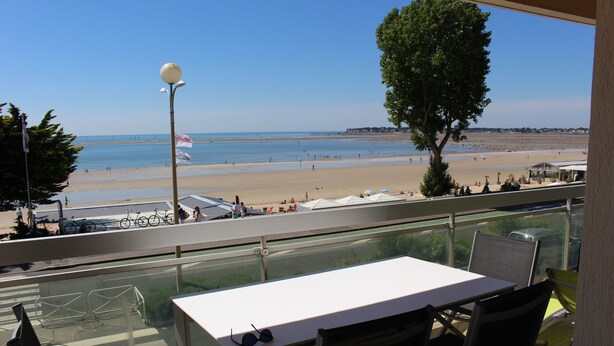 Un balcón con mesa y sillas, con vistas a una playa con tiendas de campaña y gente.