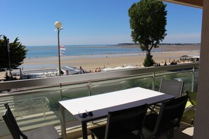 A balcony with a table and chairs, overlooking a beach with tents and people.