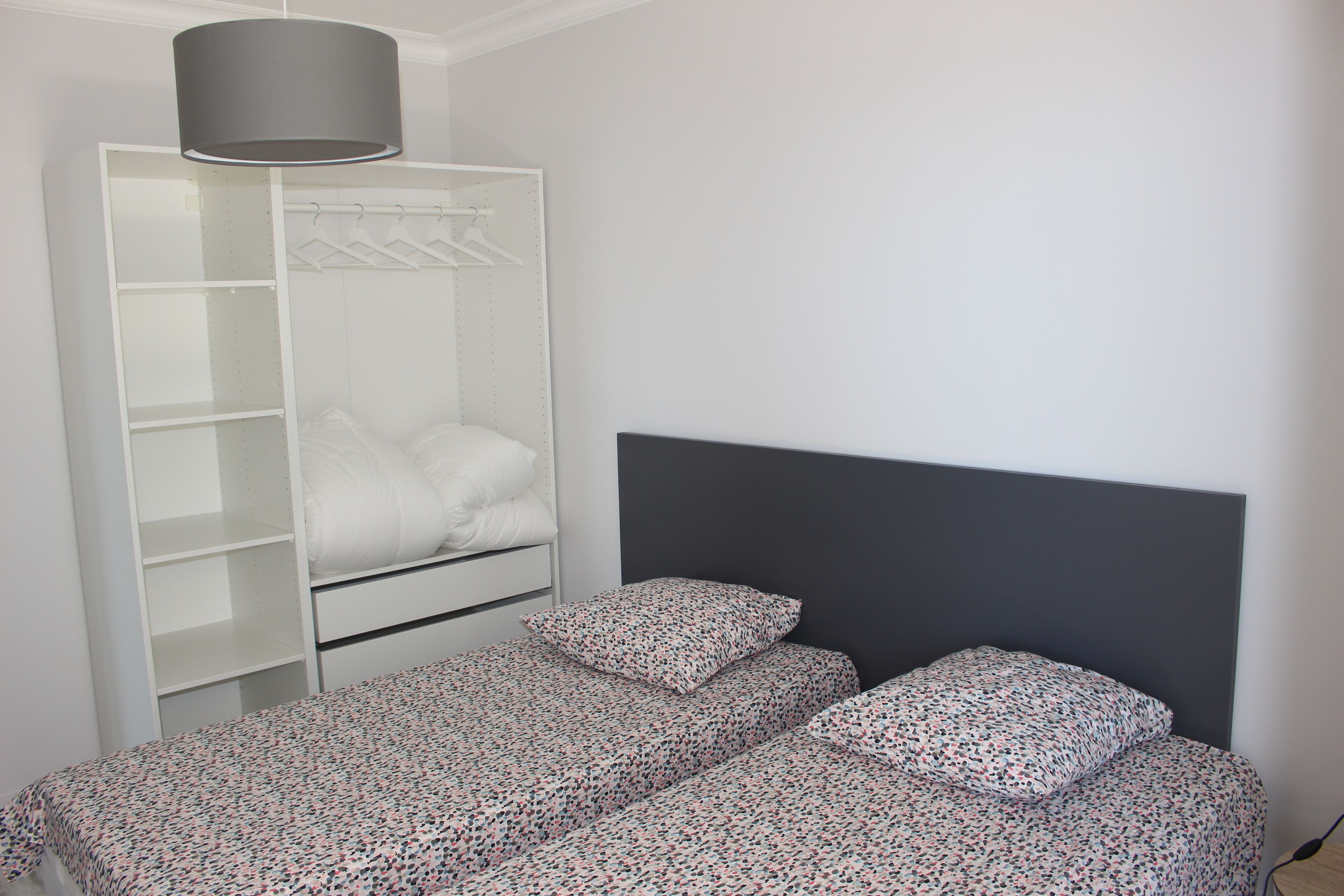 A bedroom with a bed, a wardrobe, and a hanging rack.