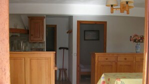 A kitchen with wooden cabinets, a dining table with a floral tablecloth, and a hanging light fixture. -  BEAUTIFUL GITE 4 PEOPLE  (Bozel)