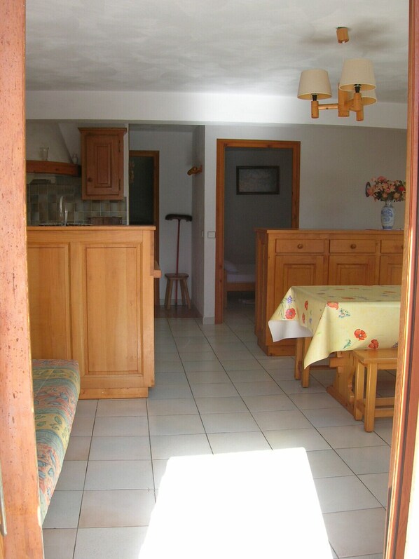 A kitchen with wooden cabinets, a dining table with a floral tablecloth, and a hanging light fixture. - BEAUTIFUL GITE 4 PEOPLE (Bozel)