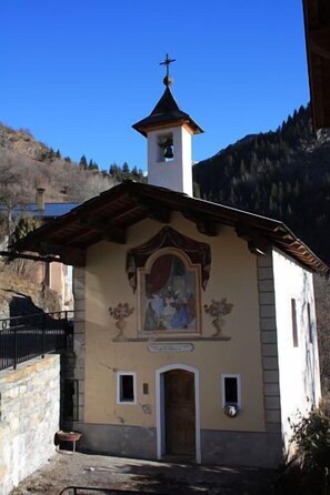 A small church with a bell tower, a fresco on the facade, and a stone wall in the background. - BEAUTIFUL GITE 4 PEOPLE (Bozel)