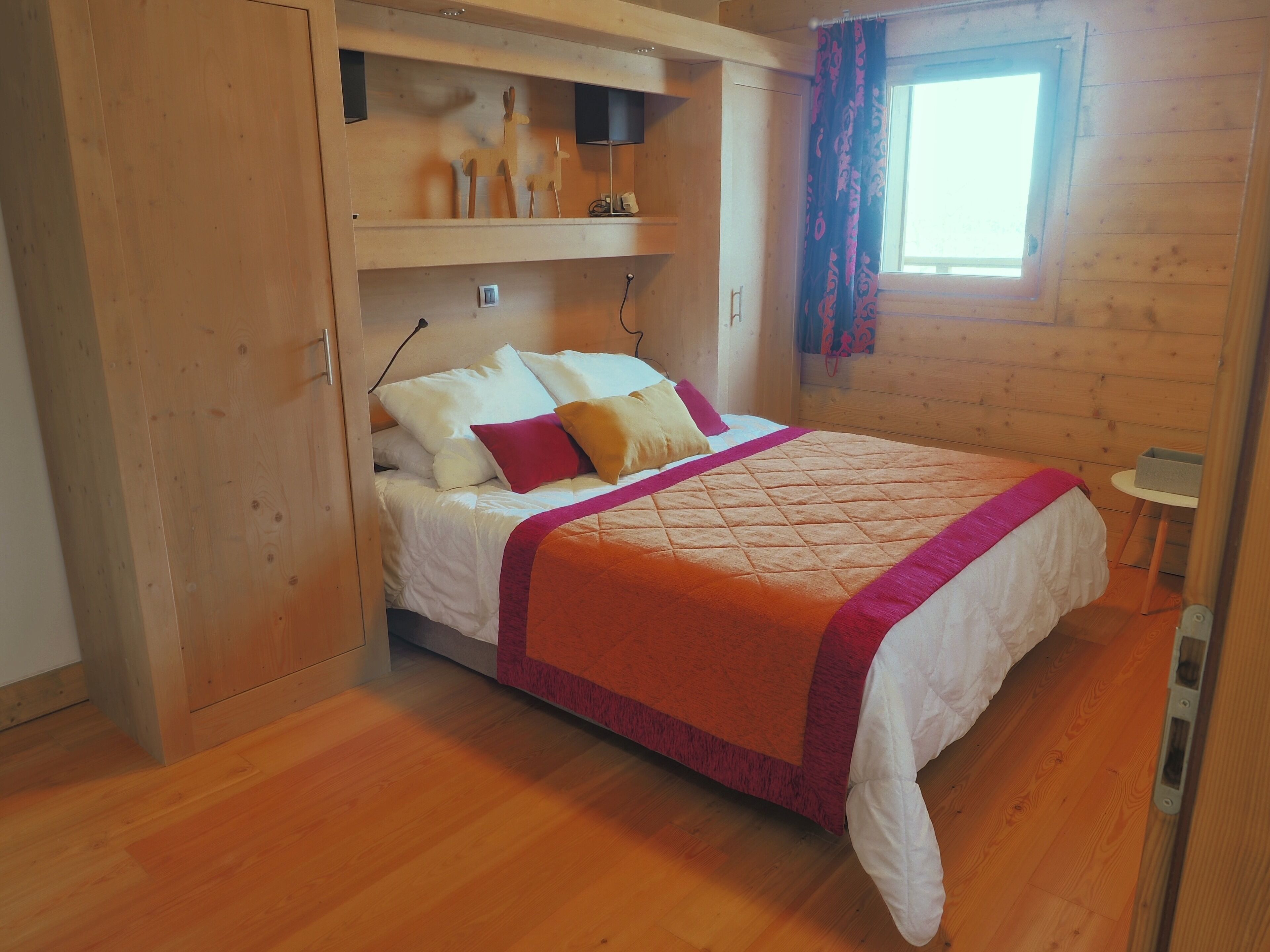 A wooden-paneled room with a bed, a small table, and a window with curtains.