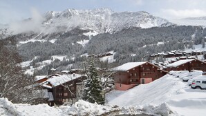 Ein schneebedecktes Bergresort mit Chalets, einer Skipiste und einem bewaldeten Tal.