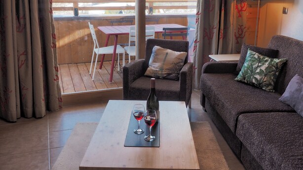 Ein gemütliches Wohnzimmer mit einem Holztisch, einer Couch und einem Balkon mit Blick auf schneebedeckte Berge.