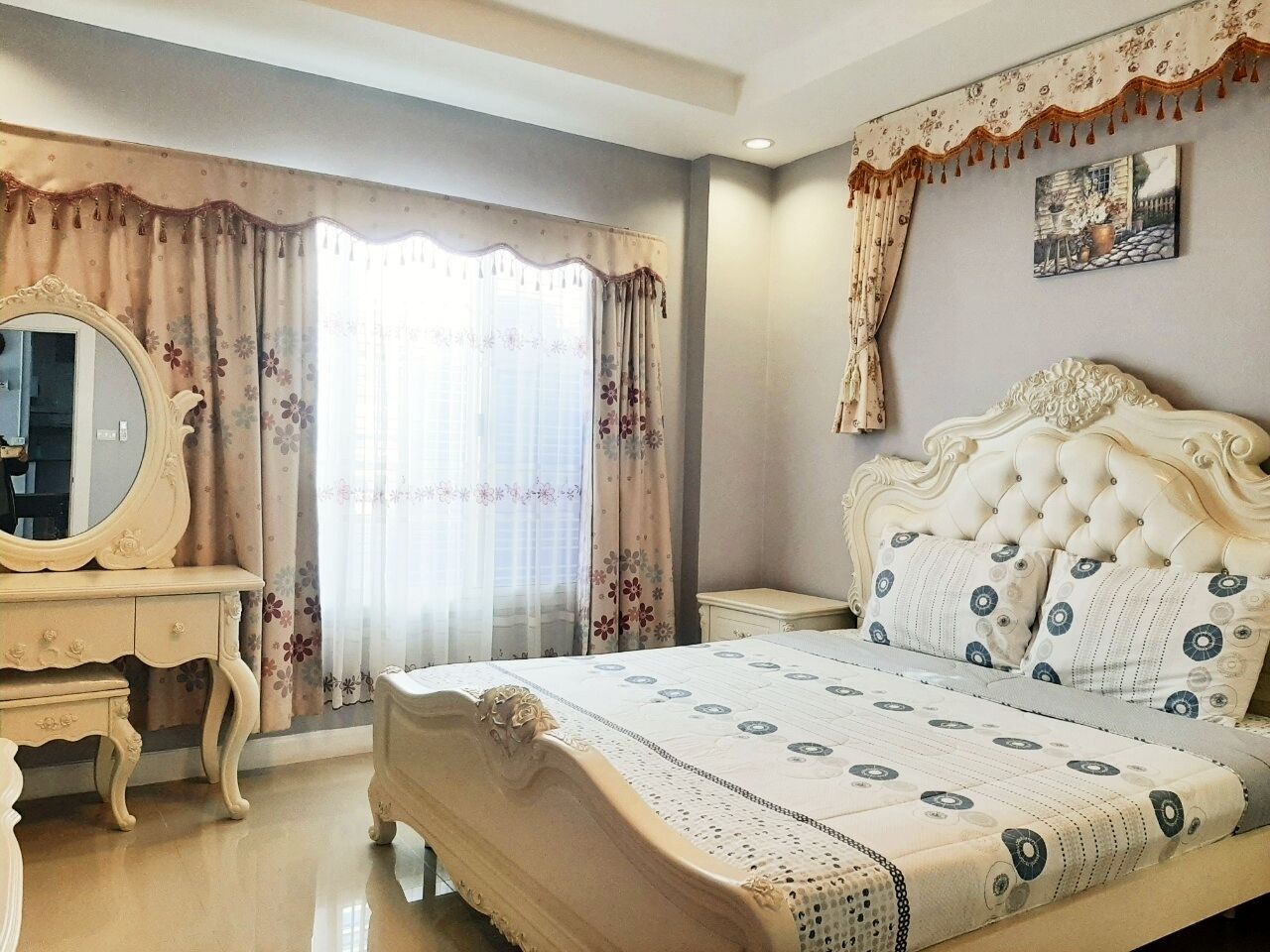 A bedroom with a large bed, a vanity with a mirror, and a window with curtains.