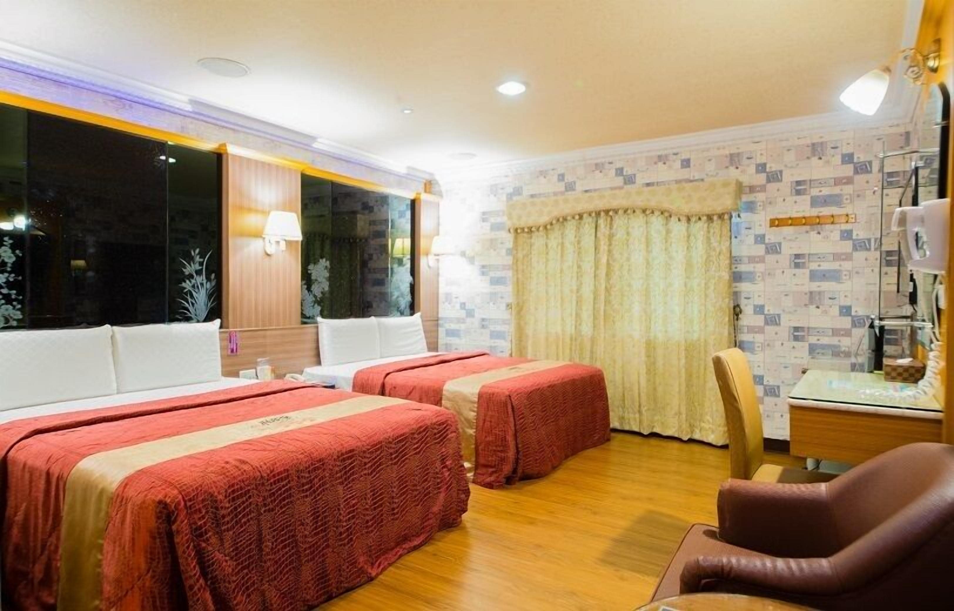A hotel room with two beds, a desk, a chair, and a window with curtains.