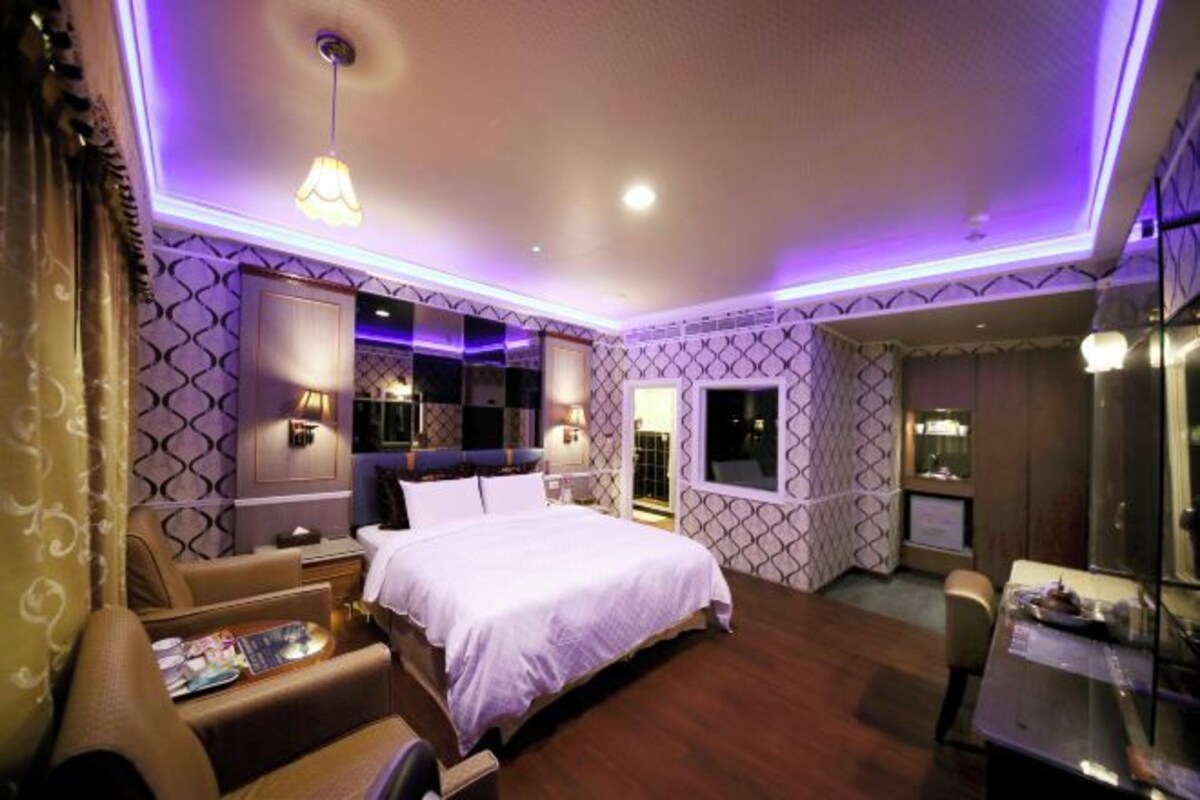A hotel room with a large bed, a sitting area with a sofa and armchair, a small desk, and a mirror.