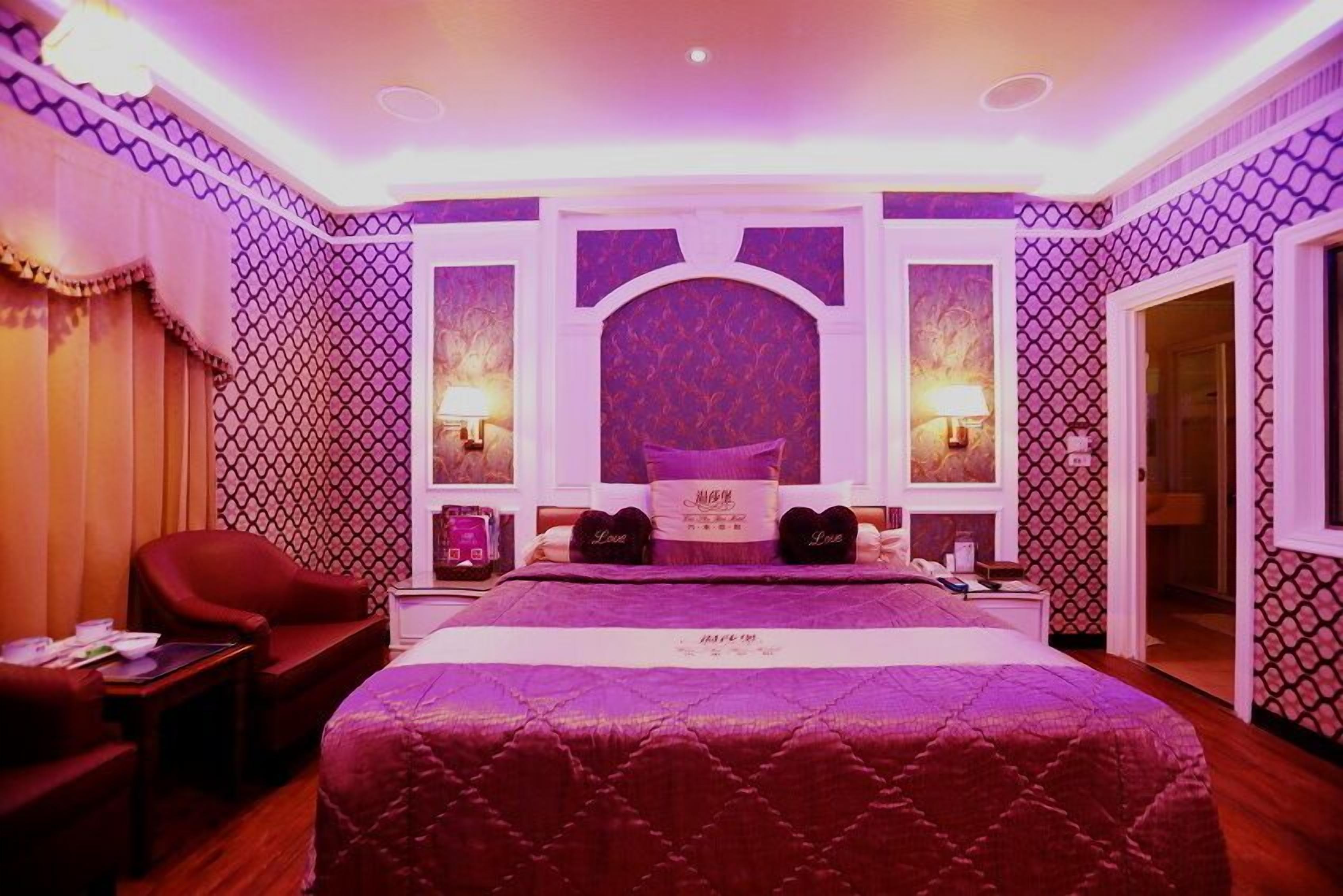 A bedroom with a large bed, two bedside lamps, a red armchair, and a small table.