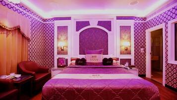 A bedroom with a large bed, two bedside lamps, a red armchair, and a small table.