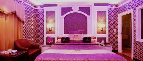 A bedroom with a large bed, two bedside lamps, a red armchair, and a small table.