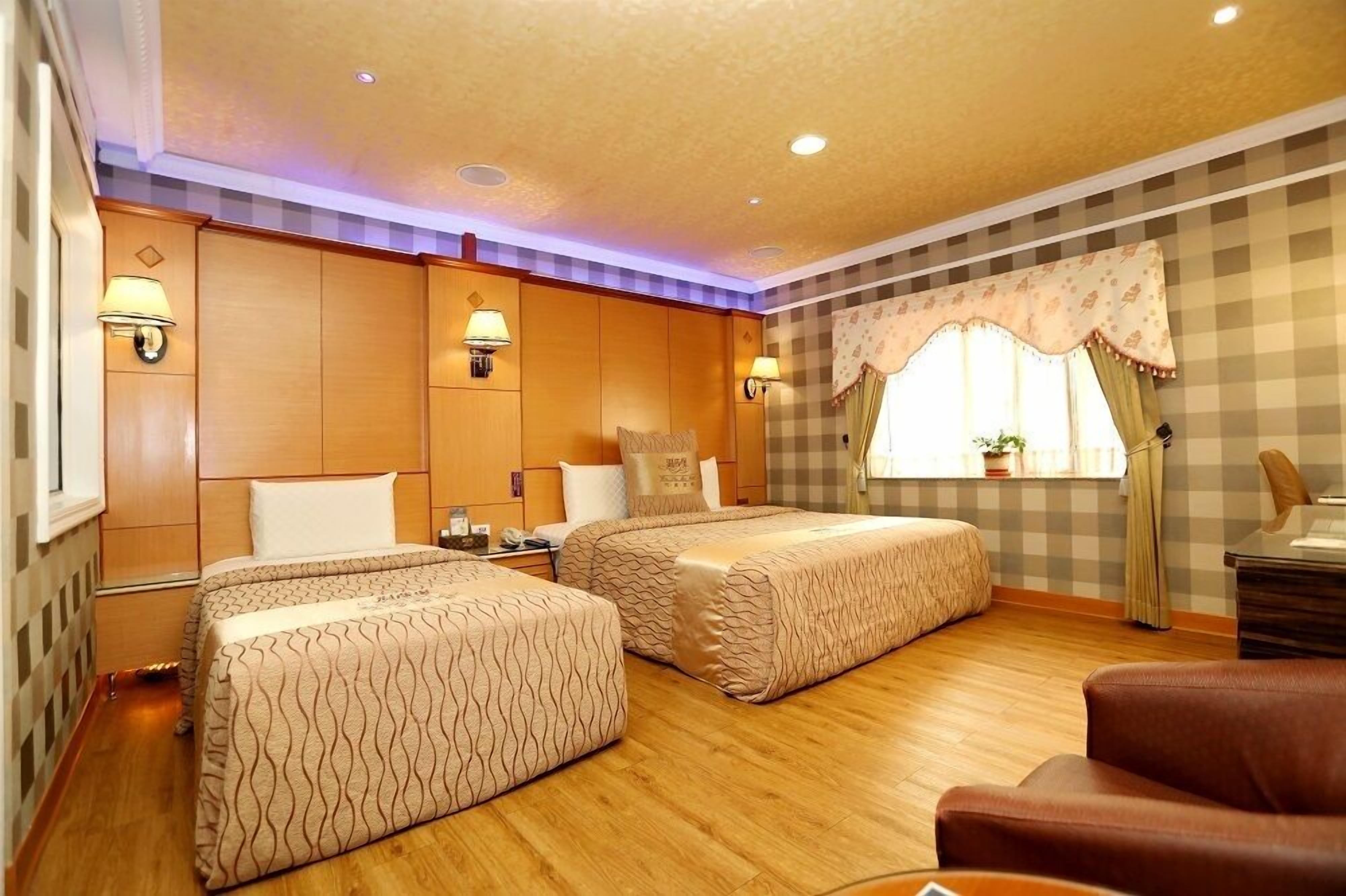 Habitación de hotel con dos camas, paneles de madera, pared a cuadros y una ventana con cortinas.