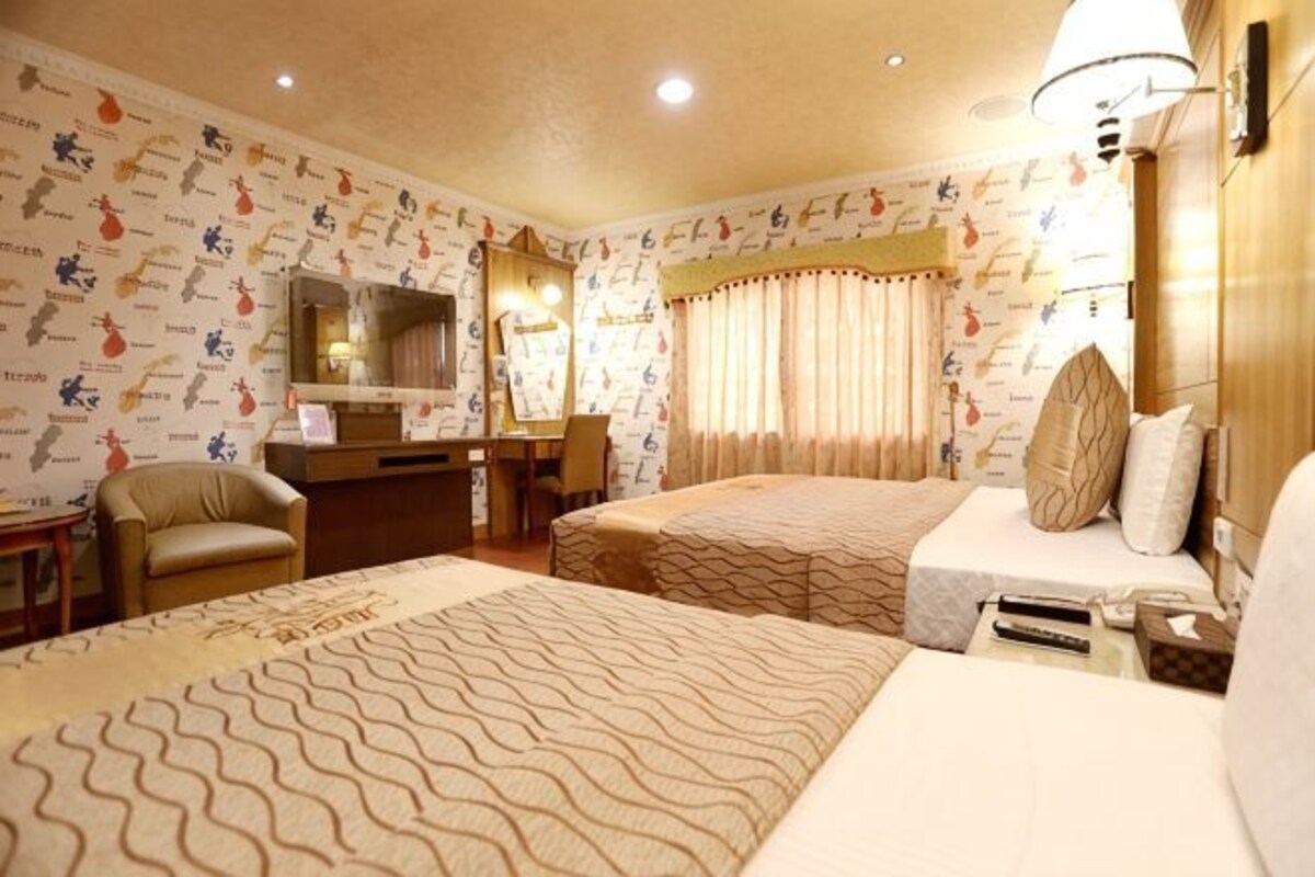 A hotel room with two beds, a desk, a chair, a mirror, and a television.