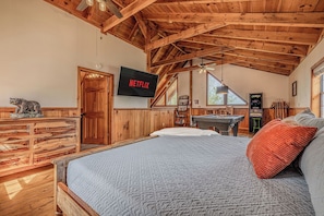 Una habitación rústica de madera con una cama, un televisor mostrando 'NETFLIX', un aparador de madera y una mesa de billar.