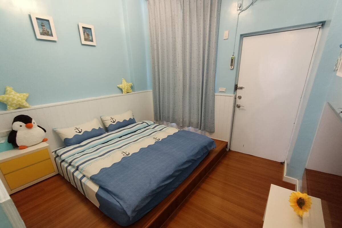 Un dormitorio con cama, mesita de noche, un peluche de pingüino y una puerta.