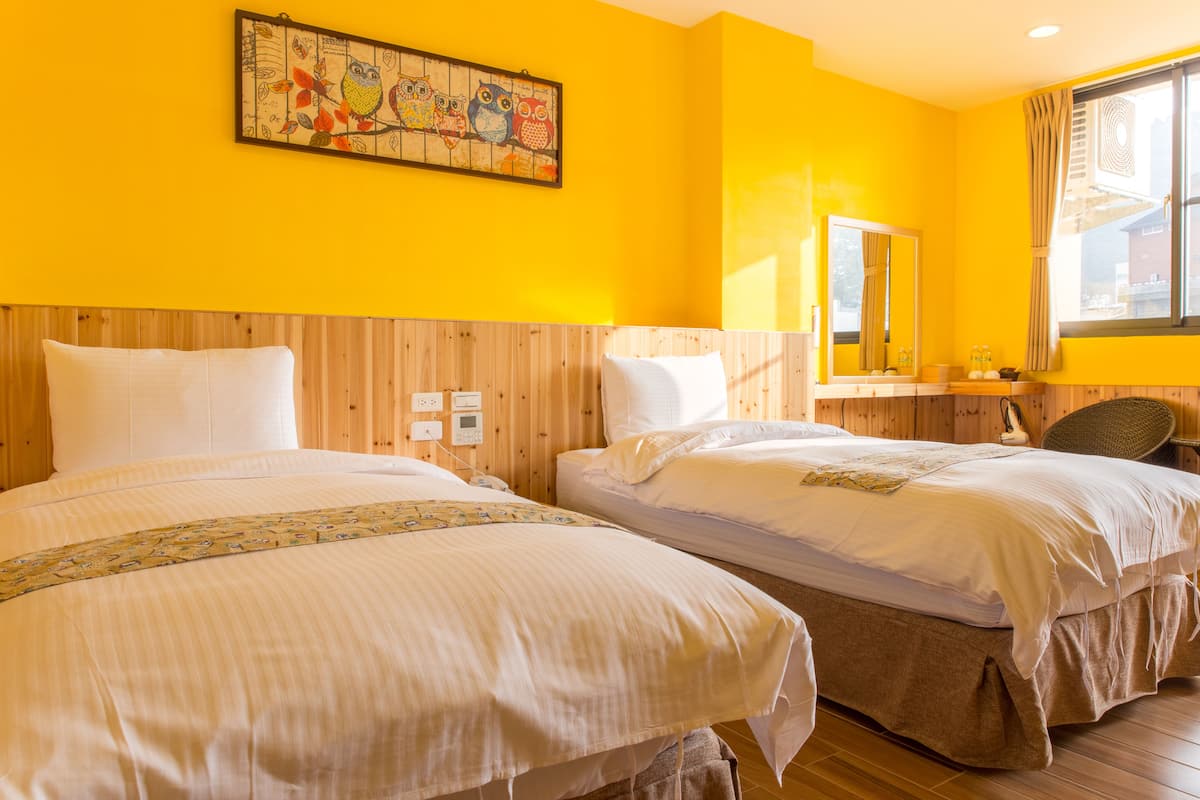 A hotel room with two beds, wooden paneling, a large window with curtains, and a wall-mounted painting.