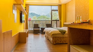 A hotel room with a bed, a small table with chairs, a TV mounted on the wall, and a balcony with a view of the mountains. - Yuan Su Inn (Yuchi)