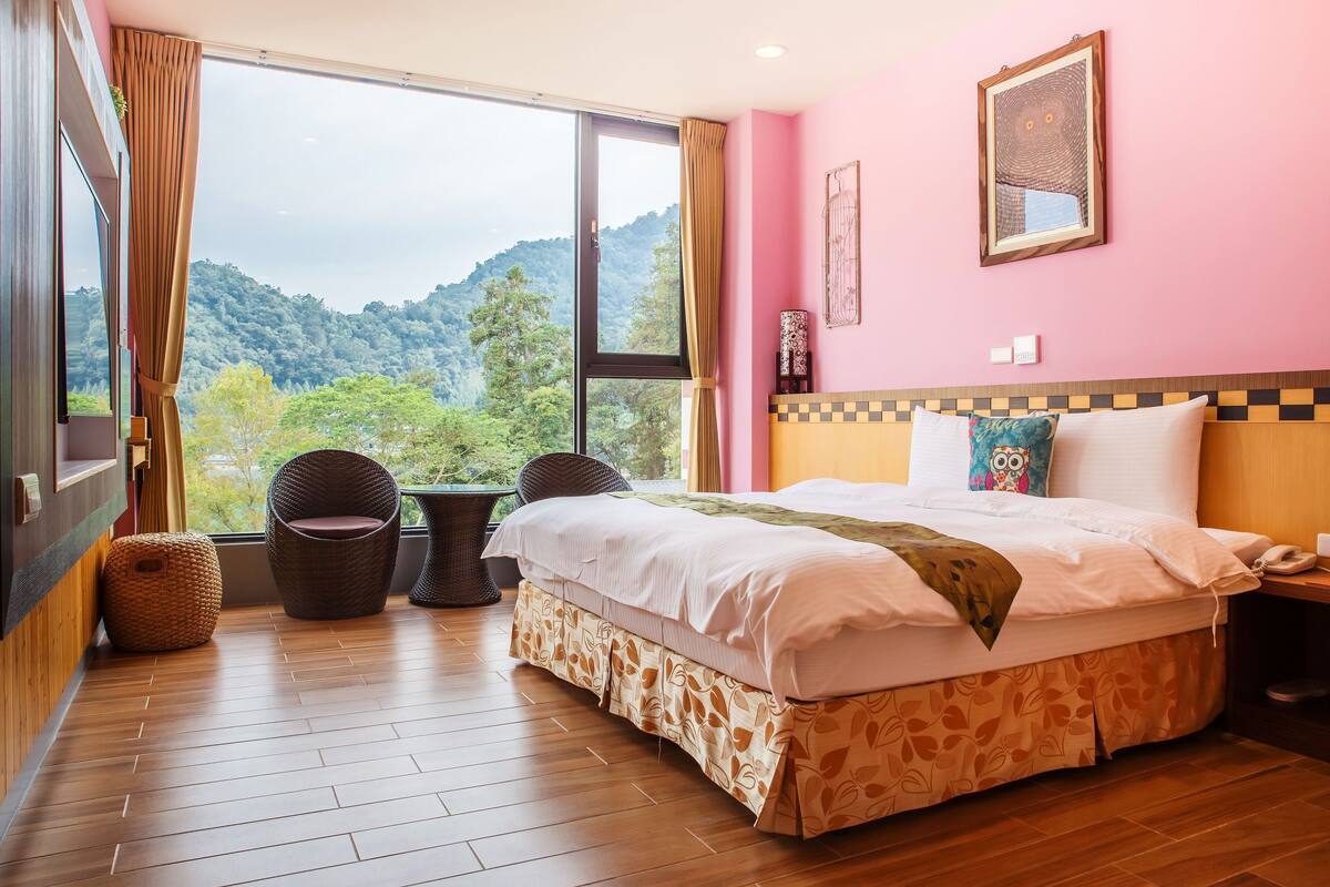 A bedroom with a large window, a bed, a chair, and a small table.