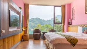 A hotel room with a bed, a television, wicker chairs, and a view of a mountainous landscape. - Yuan Su Inn (Yuchi)