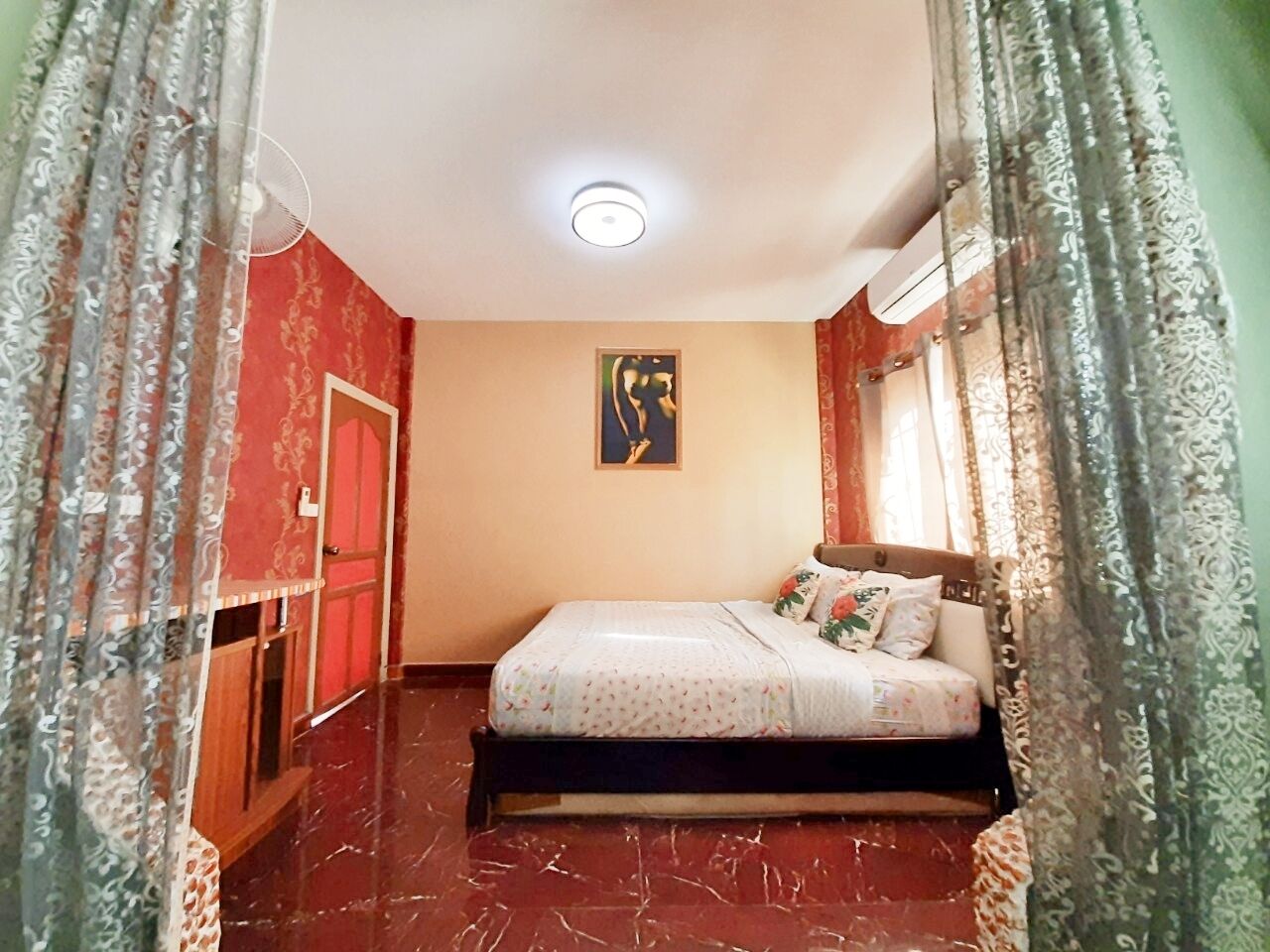 A bedroom with a bed, a ceiling fan, a painting, and a wardrobe.