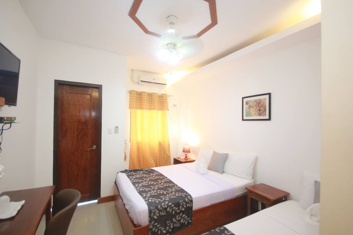 A hotel room with a bed, a desk, a chair, a nightstand, a lamp, a picture on the wall, and a ceiling fan.