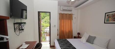 Habitación de hotel con cama, escritorio, silla, televisor, aire acondicionado y ventana con cortinas.