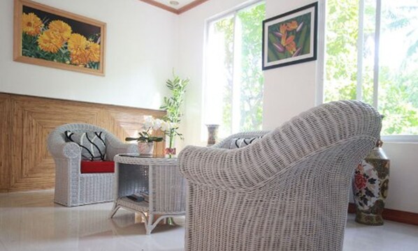 A room with wicker furniture, a wooden headboard, and a window with a view of greenery.