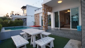 A modern outdoor patio with a pool, white furniture, and a glass door leading to a living area. - Baan Rolita Pool Villa Hua Hin (Hua Hin)