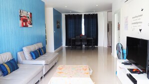 A modern living room with a sofa, a dining table with chairs, a TV, and a fan. - Baan Rolita Pool Villa Hua Hin (Hua Hin)