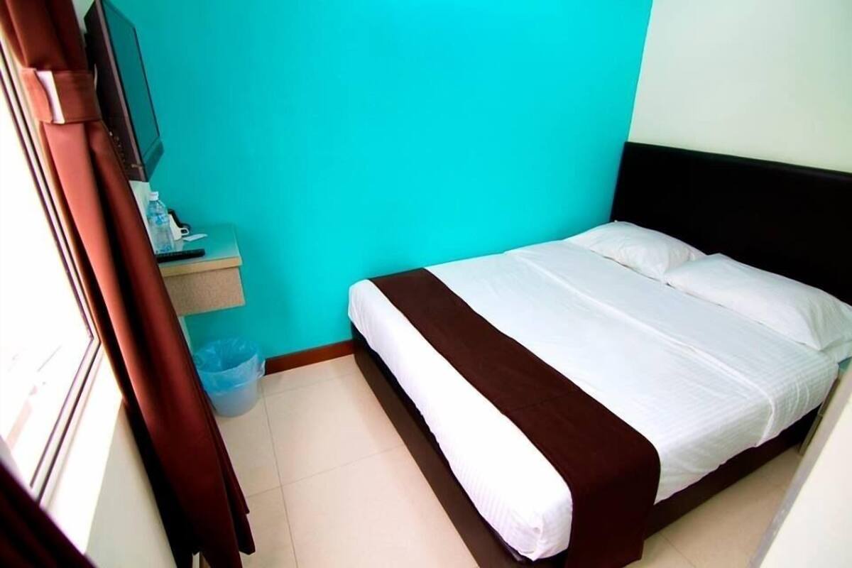Una cama individual con ropa de cama blanca y marrón en una habitación con paredes turquesa y suelo de madera.