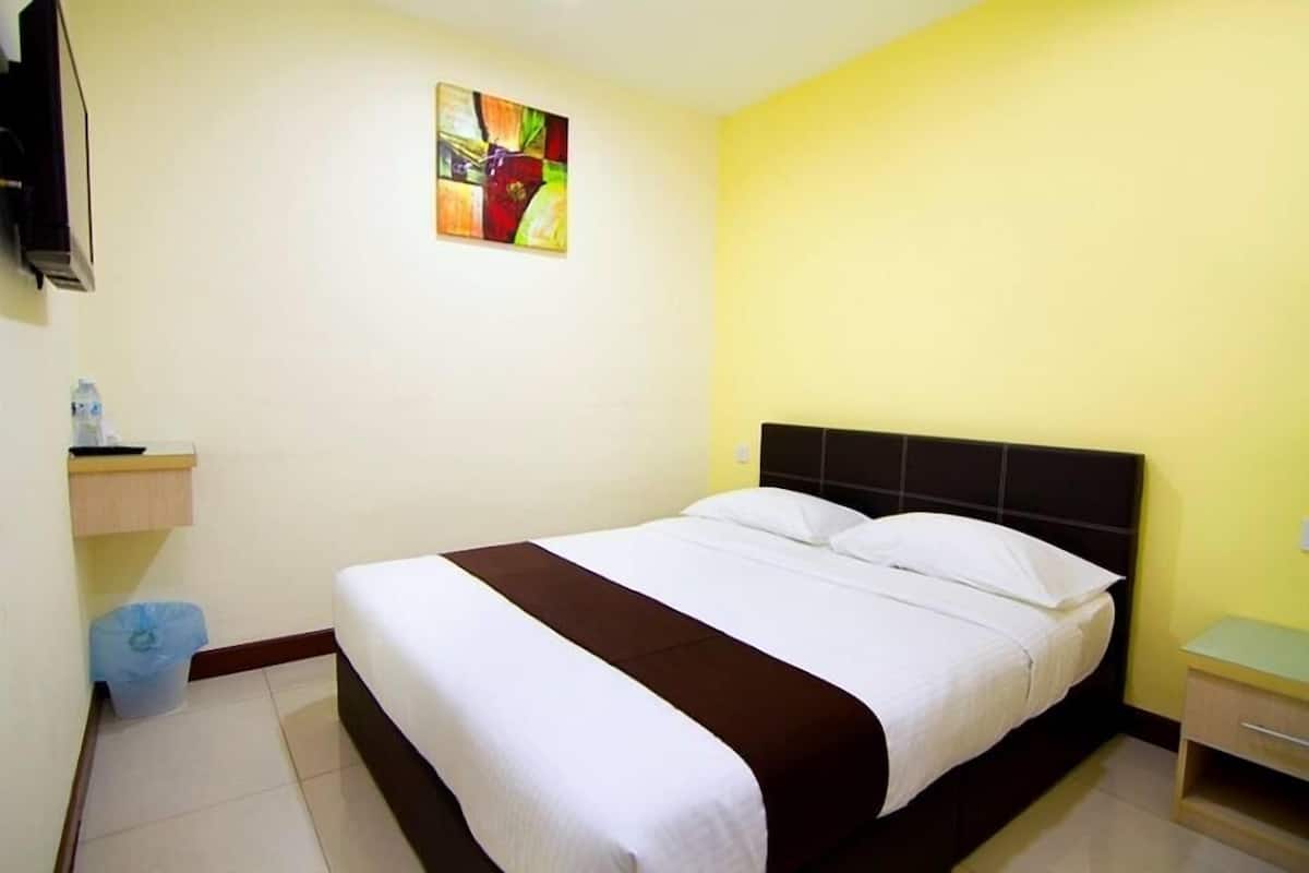 Una habitación de hotel con cama, mesita de noche, cubo de basura y televisor de pared.