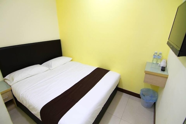 A single bed with white and brown bedding, a small bedside table, a trash bin, and a shelf with bottled water and a remote control. - Sg Pelek Hotel (Sungai Pelek)
