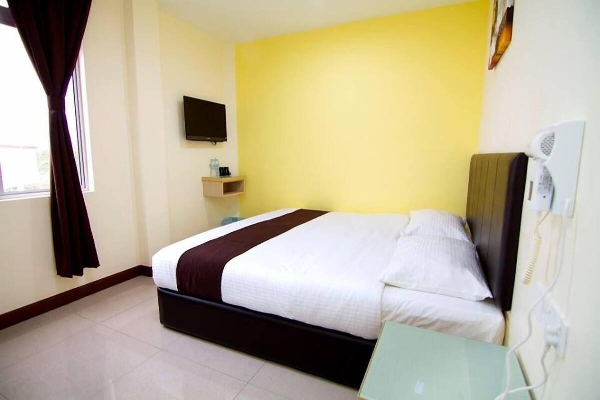 Habitación de hotel con cama, televisor montado en la pared y mesita de noche con lámpara.
